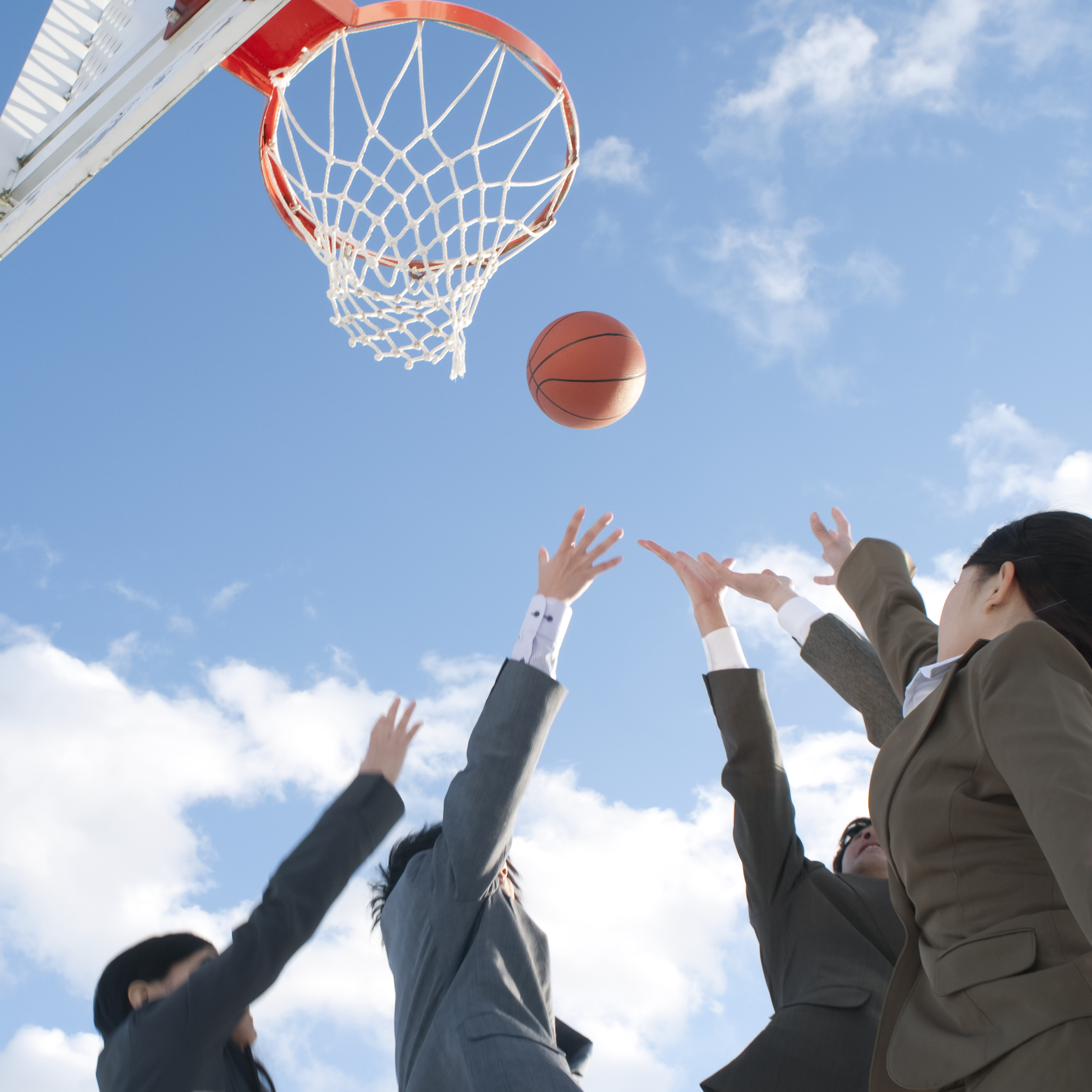 Photo of people in business suits reaching up toward a basketball that is in the air near a basketball hoop.