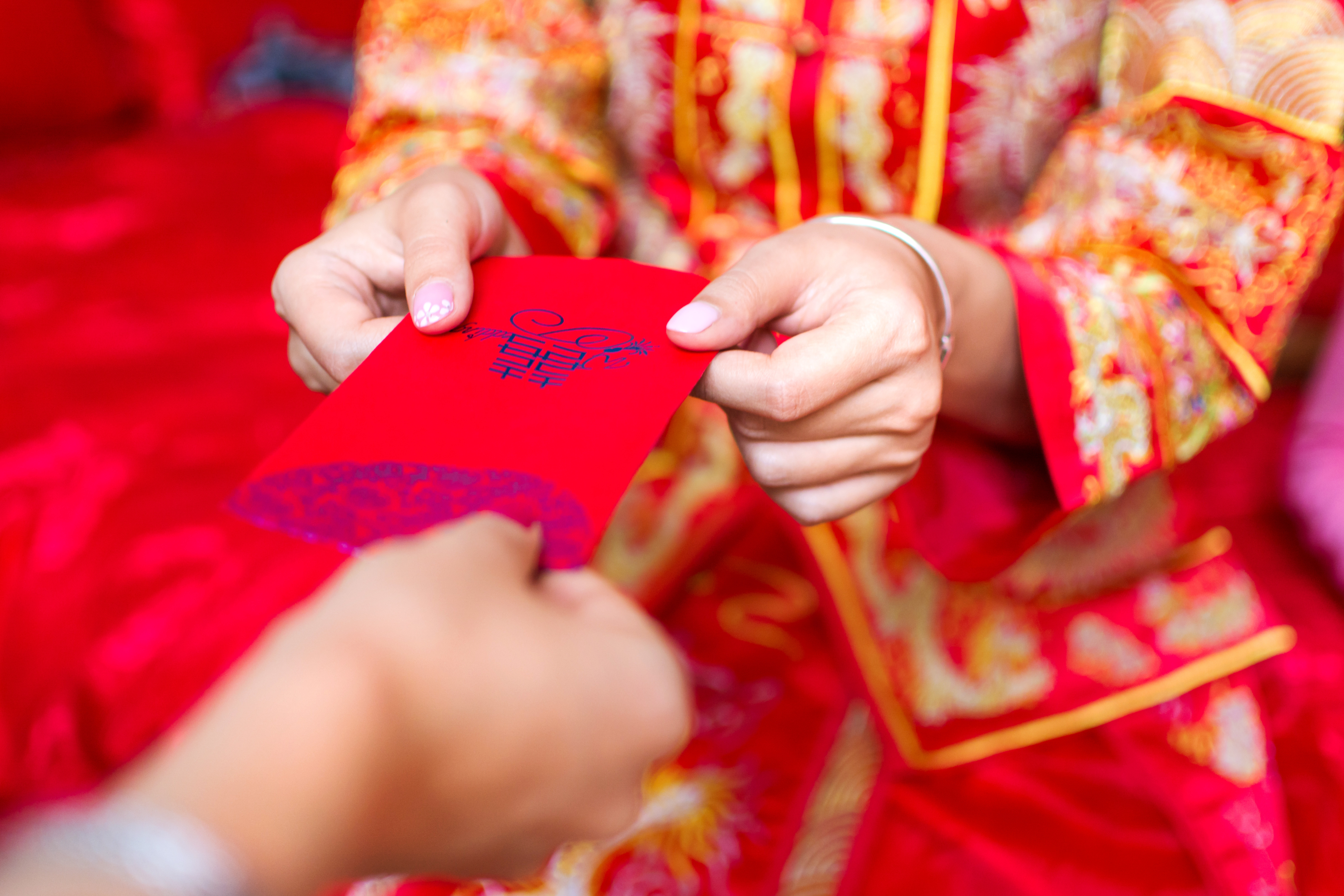 Person in bright embroidered red and yellow clothing handing red envelope to another persion.