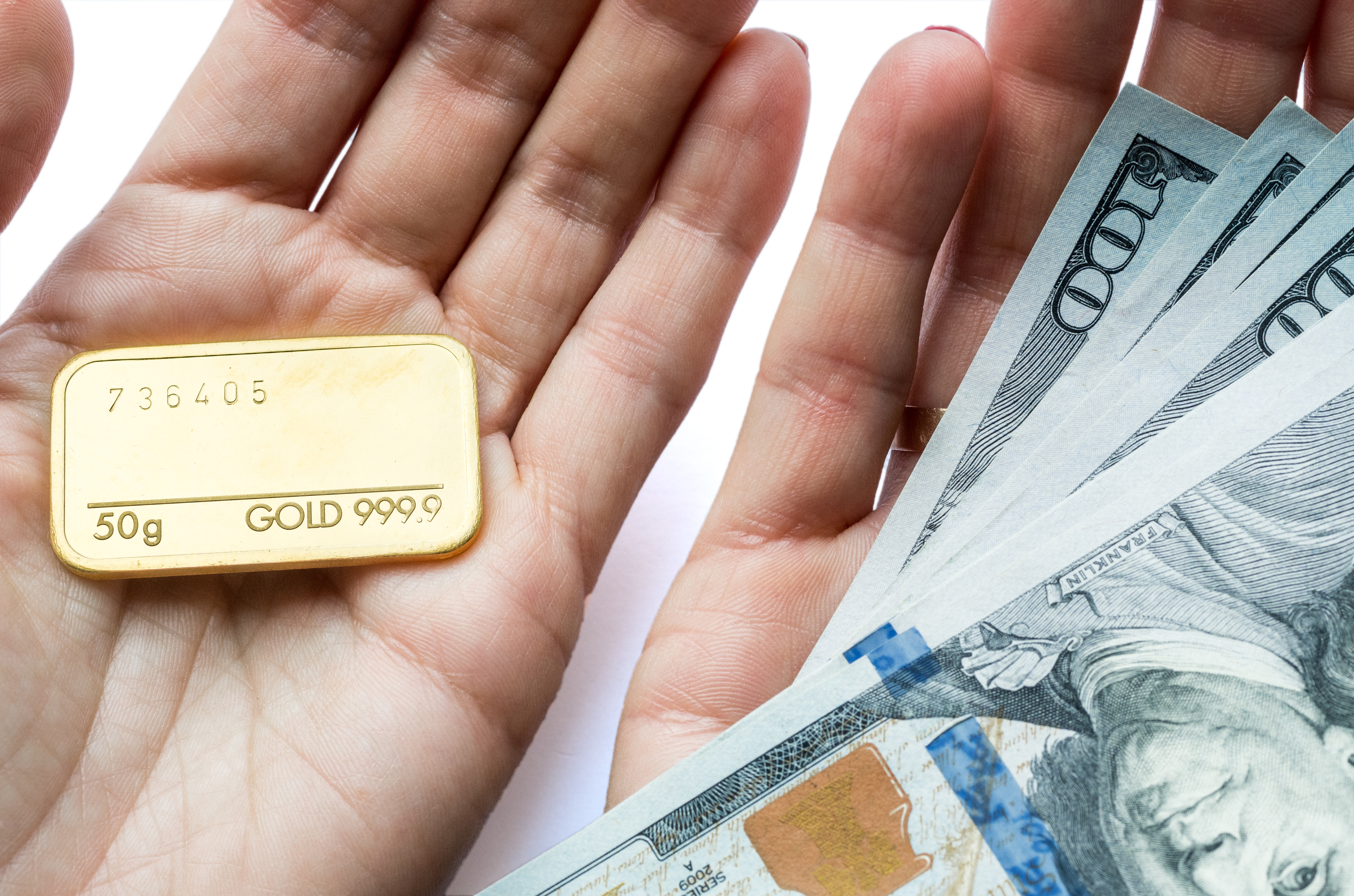 Person holding gold bullion in one hand and $100 bills in the other.