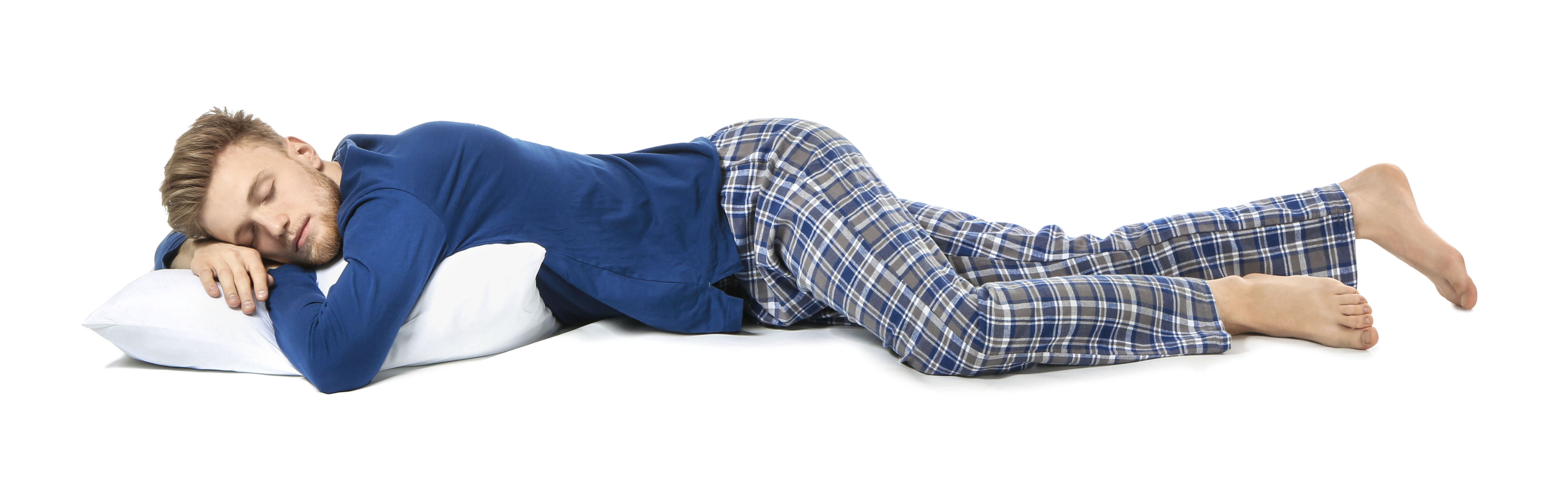 Image of a young man in a blut t-shirt and blue/gray plaid pajama pants lying asleep on a white pillow. Background of image is white.