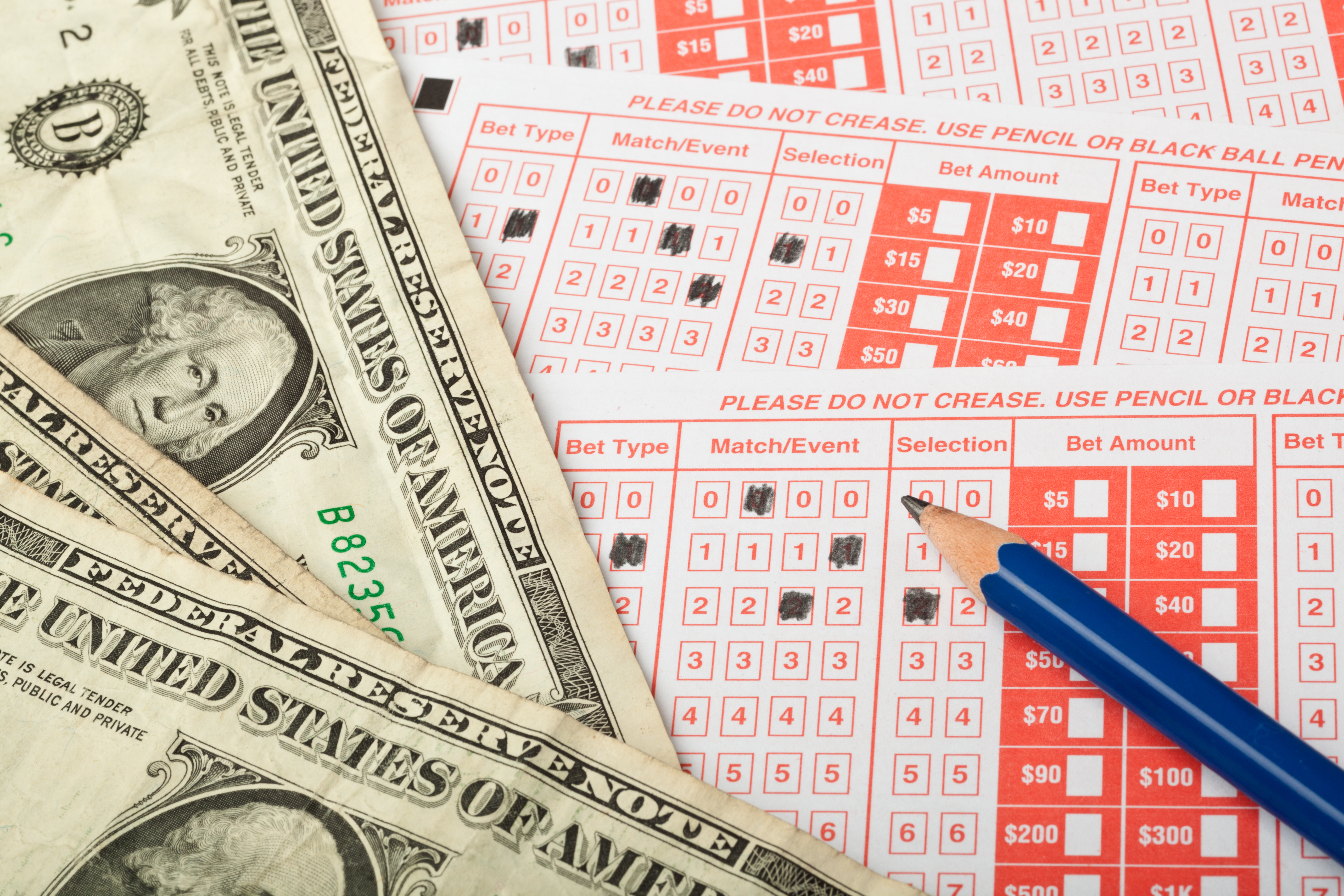 Dollar bills and a blue pencil lying on top of red-and-white bettin slips.