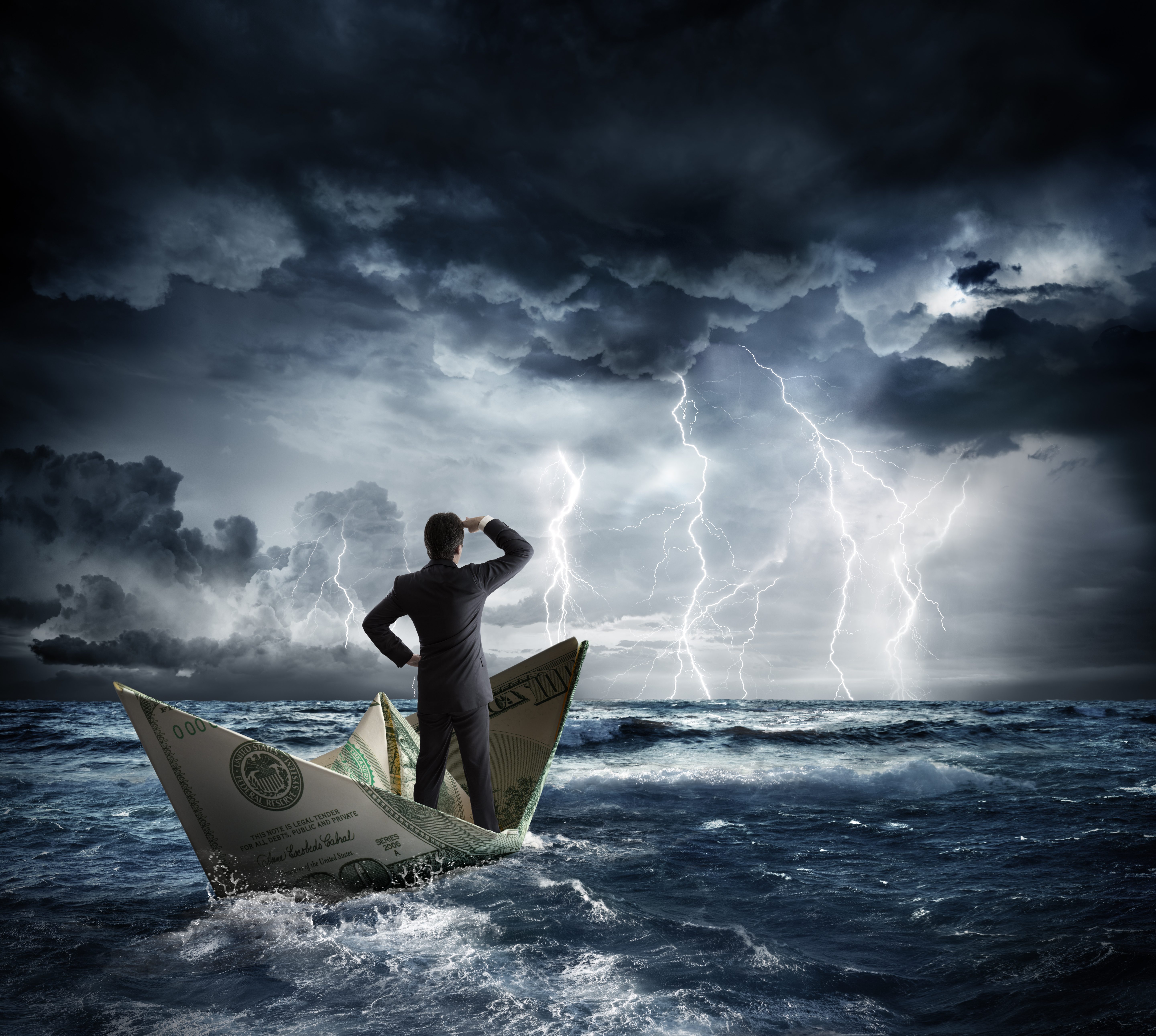 Photo-illustration: a person in a business suit stands in a boat made of a folded $100 bill, surveying lightning, thunderclouds, and rough seas ahead.