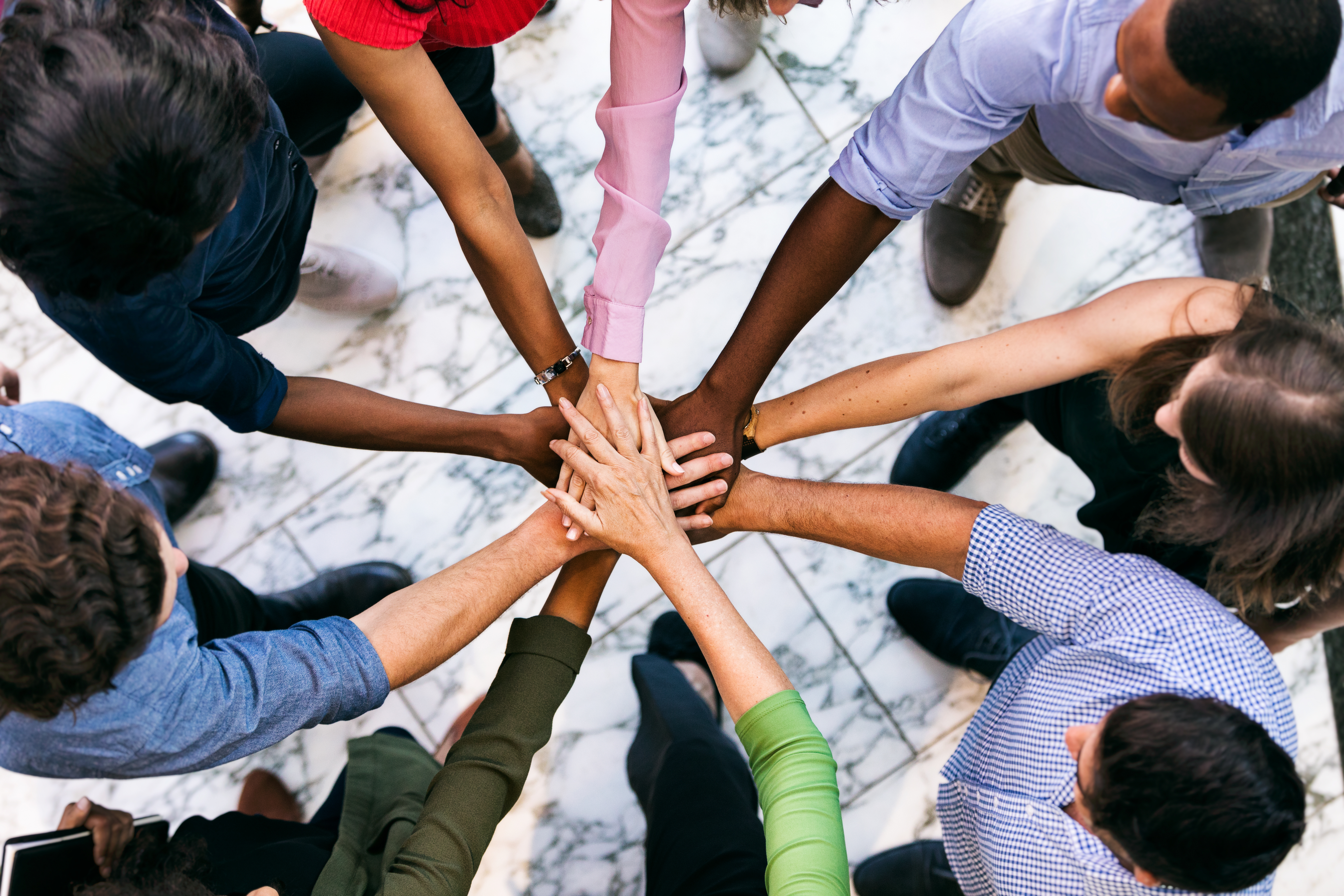 Diverse group of people standing together in a circle, with their hands meeting in the center.