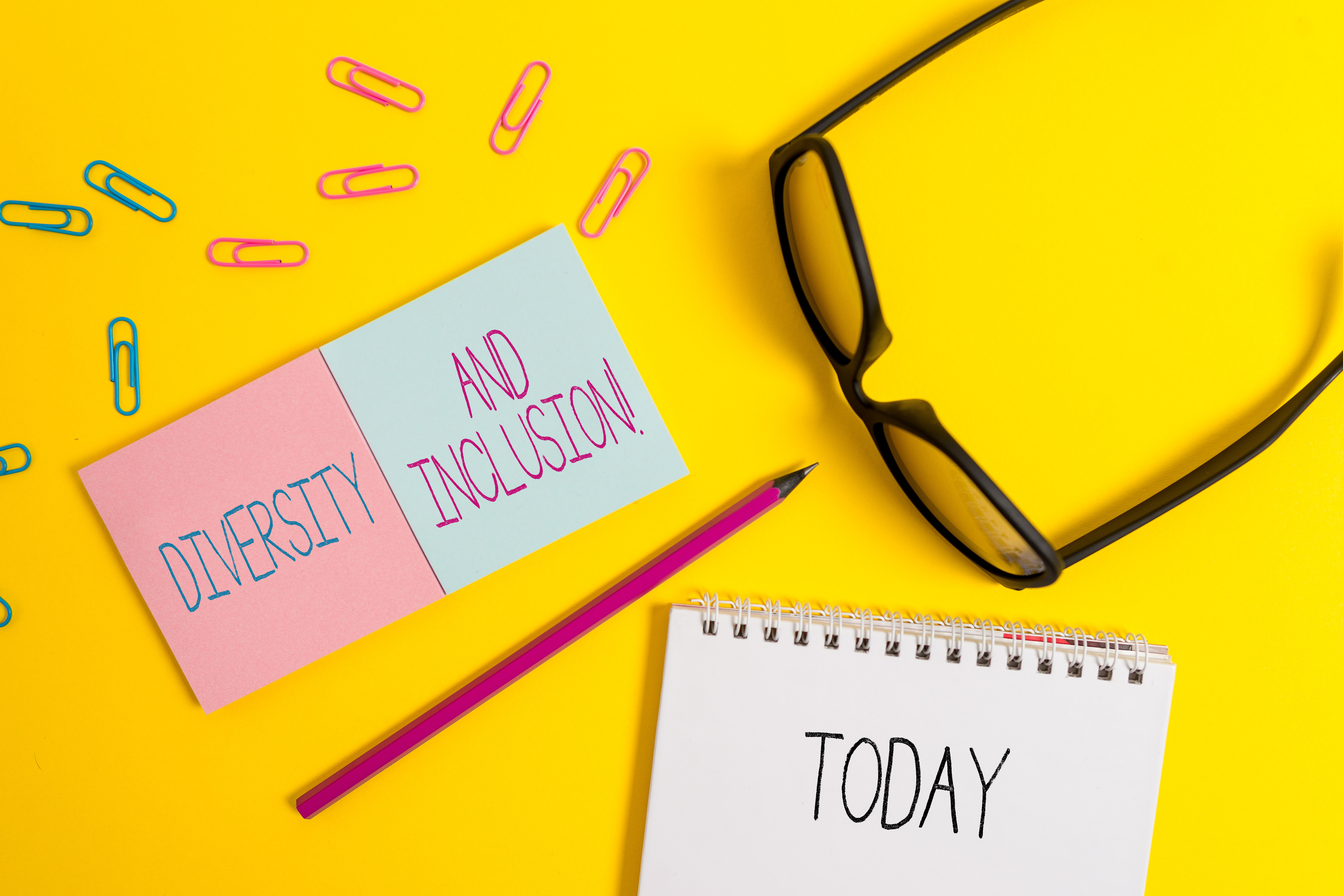 Yellow background with glasses, pencil, paper clips, and notepads saying, "DIVERSITY AND INCLUSION TODAY!"