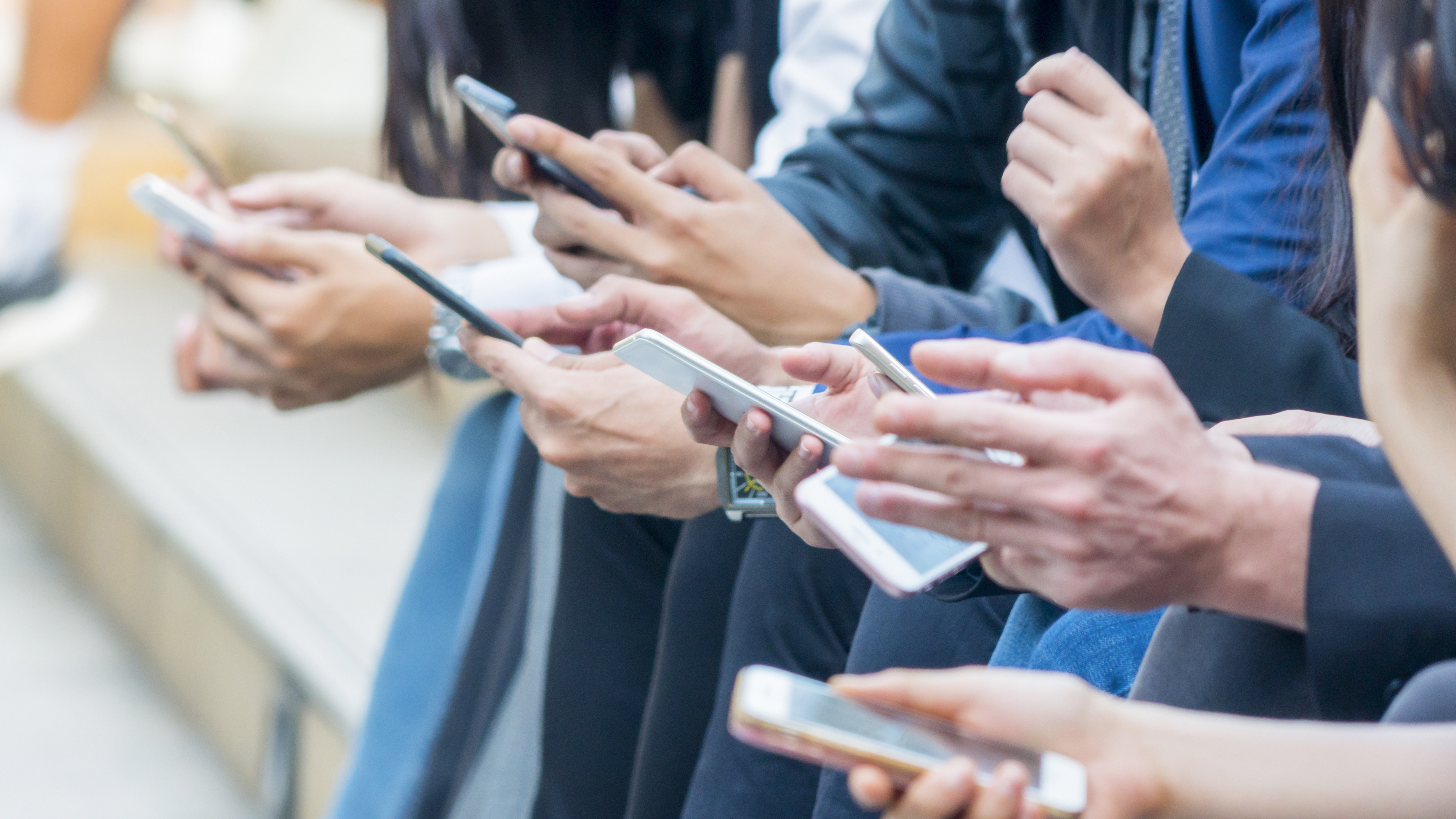 Hands of many people using their smartphones.