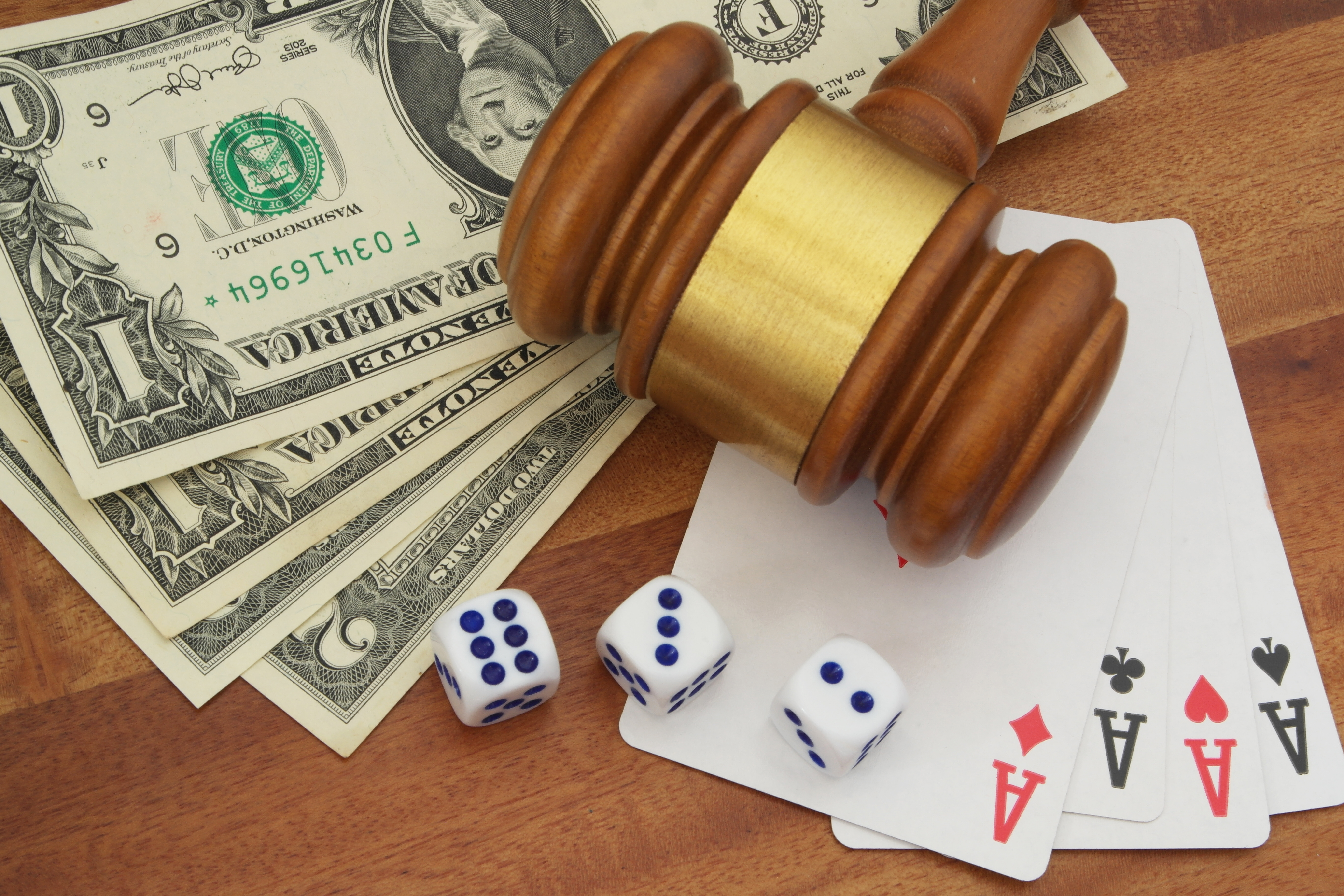 Gavel lying on top of cash and playing cards, with dice nearby.