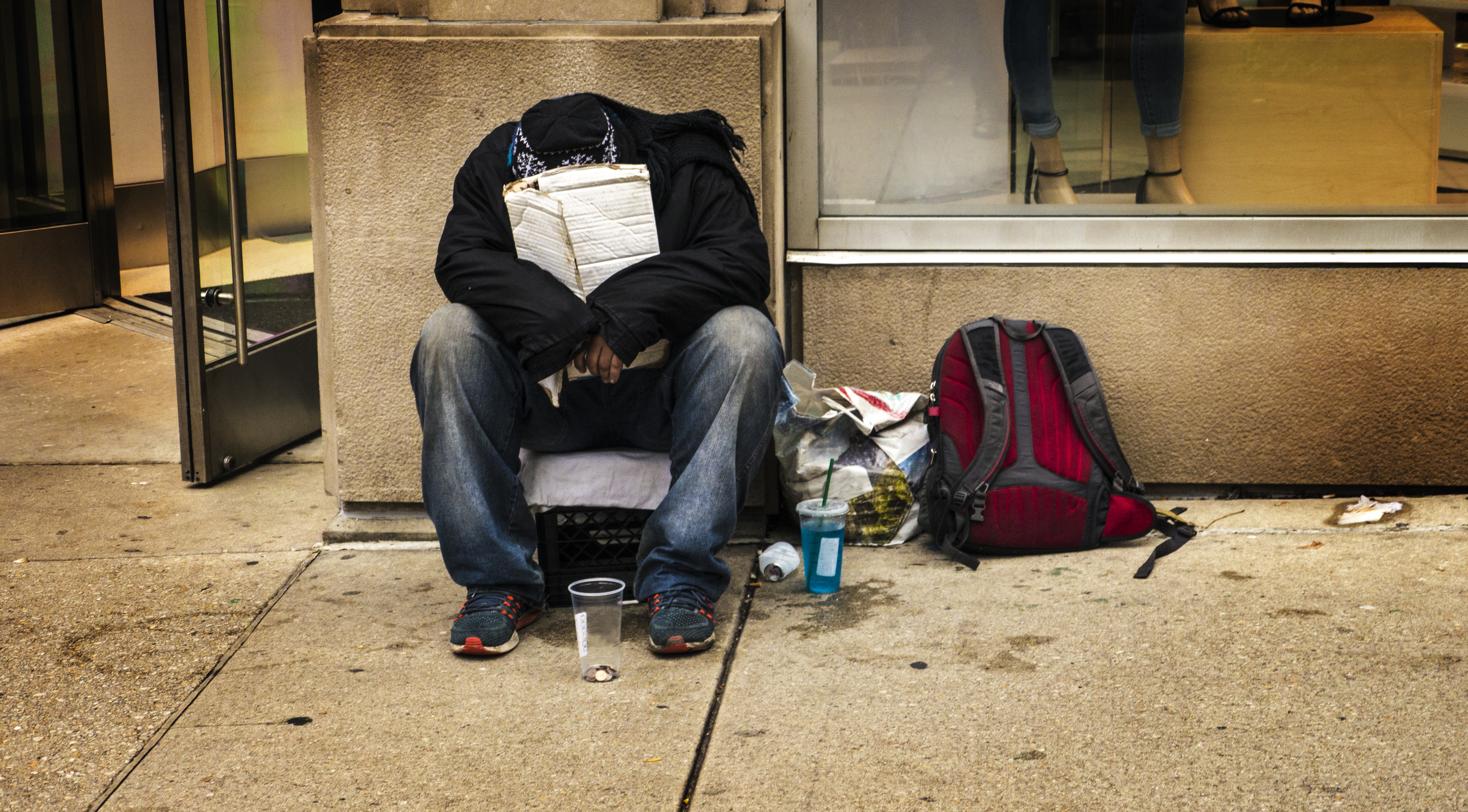 Homeless person sitting on city sidewalk.