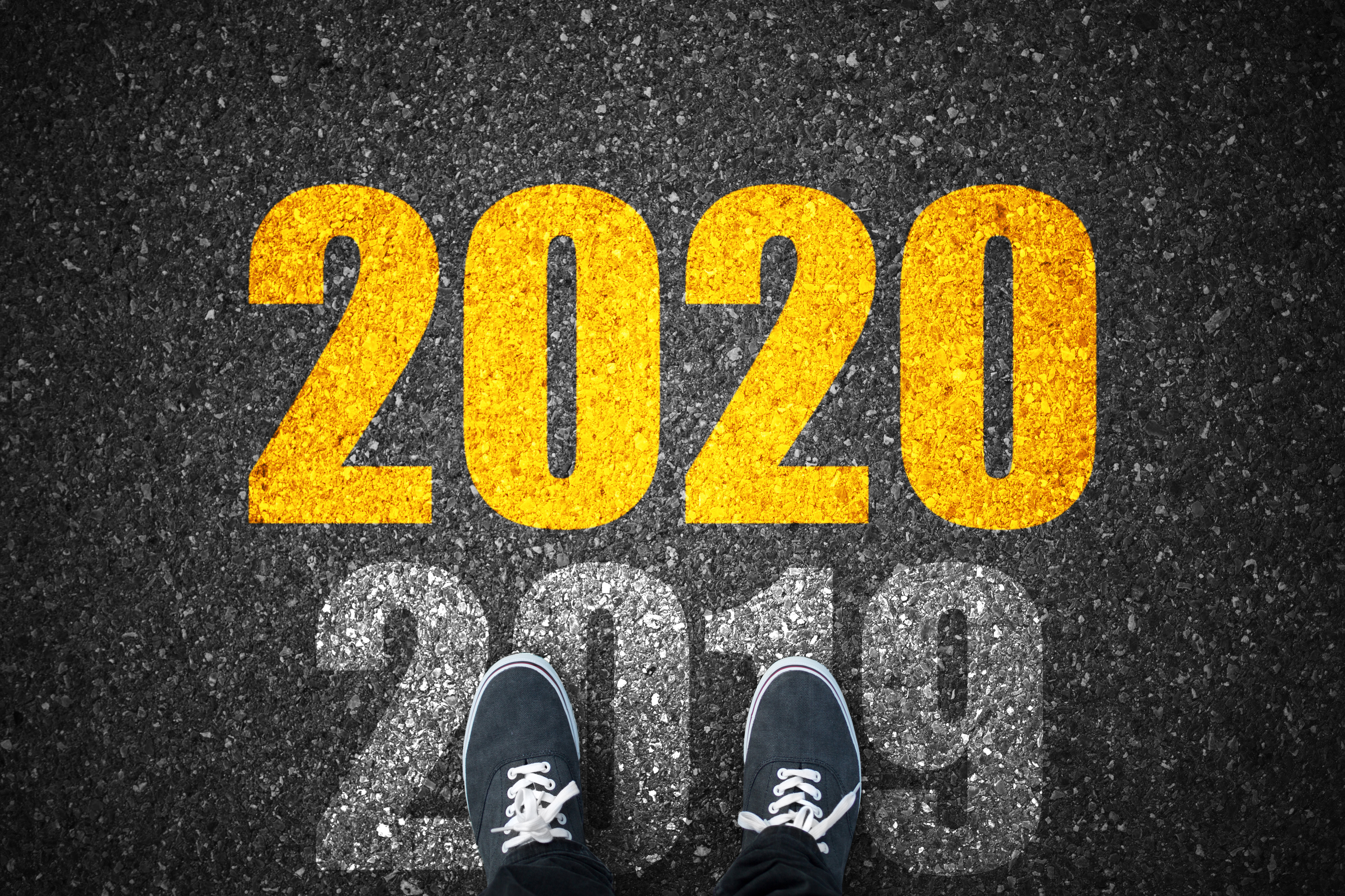 View downward at person's feet standing on top of faded gray "2019" with bright gold "2020" in front of them.