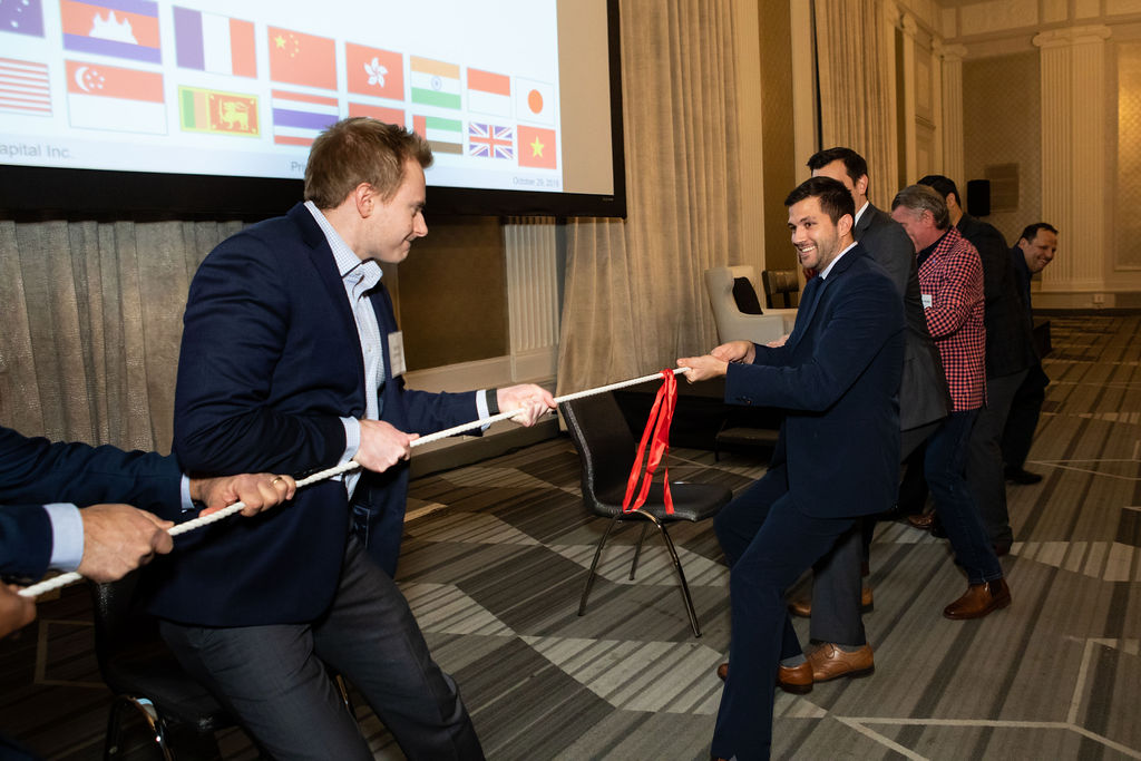 Two teams of people in business attire square off across a tug-of-war rope at a conference.