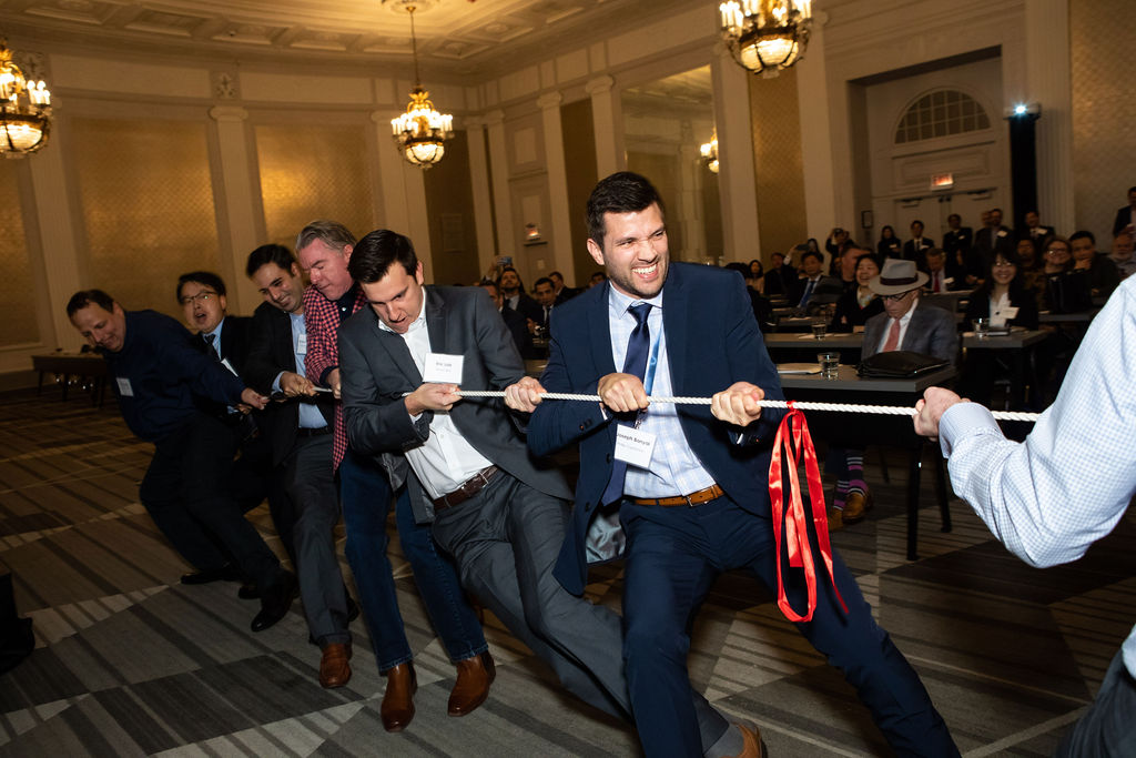 People in business attire pulling on tug-of-war rope at a conference.